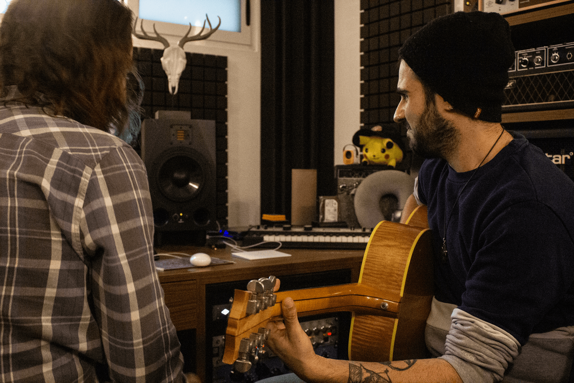 A tutor playing acoustic guitar beside a student in a one-to-one session at the AISO studio