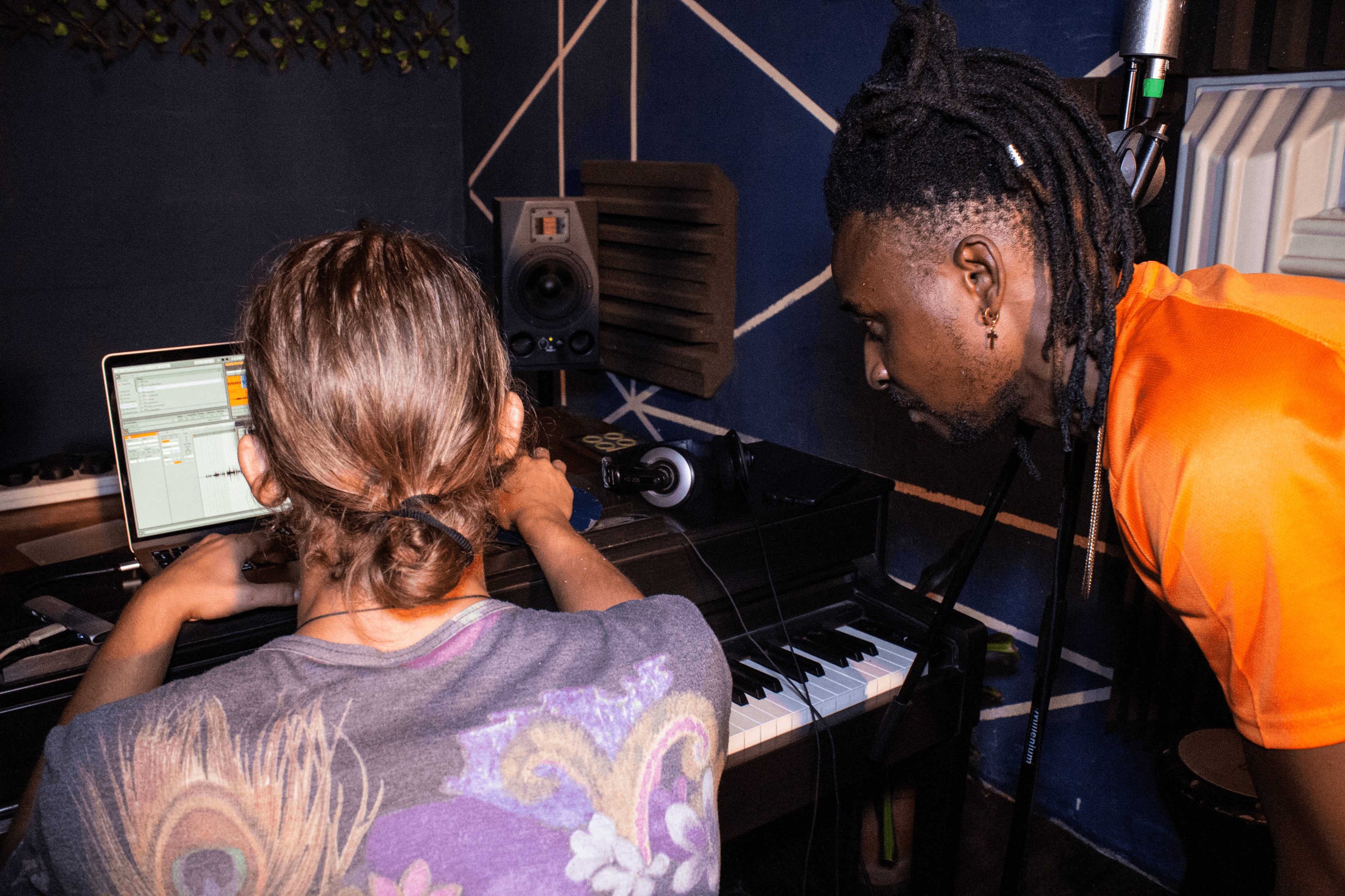 Two producers arranging a track in Ableton Live beside an upright piano in the AISO studio