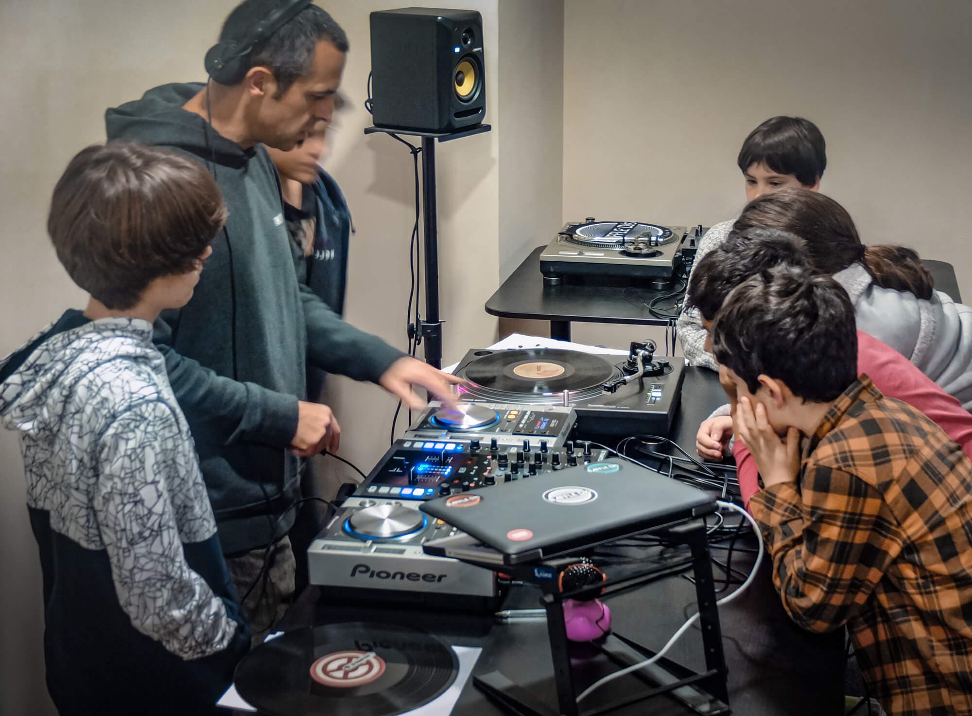 An AISO instructor teaching a group of kids on Pioneer DJ controllers and turntables in a classroom