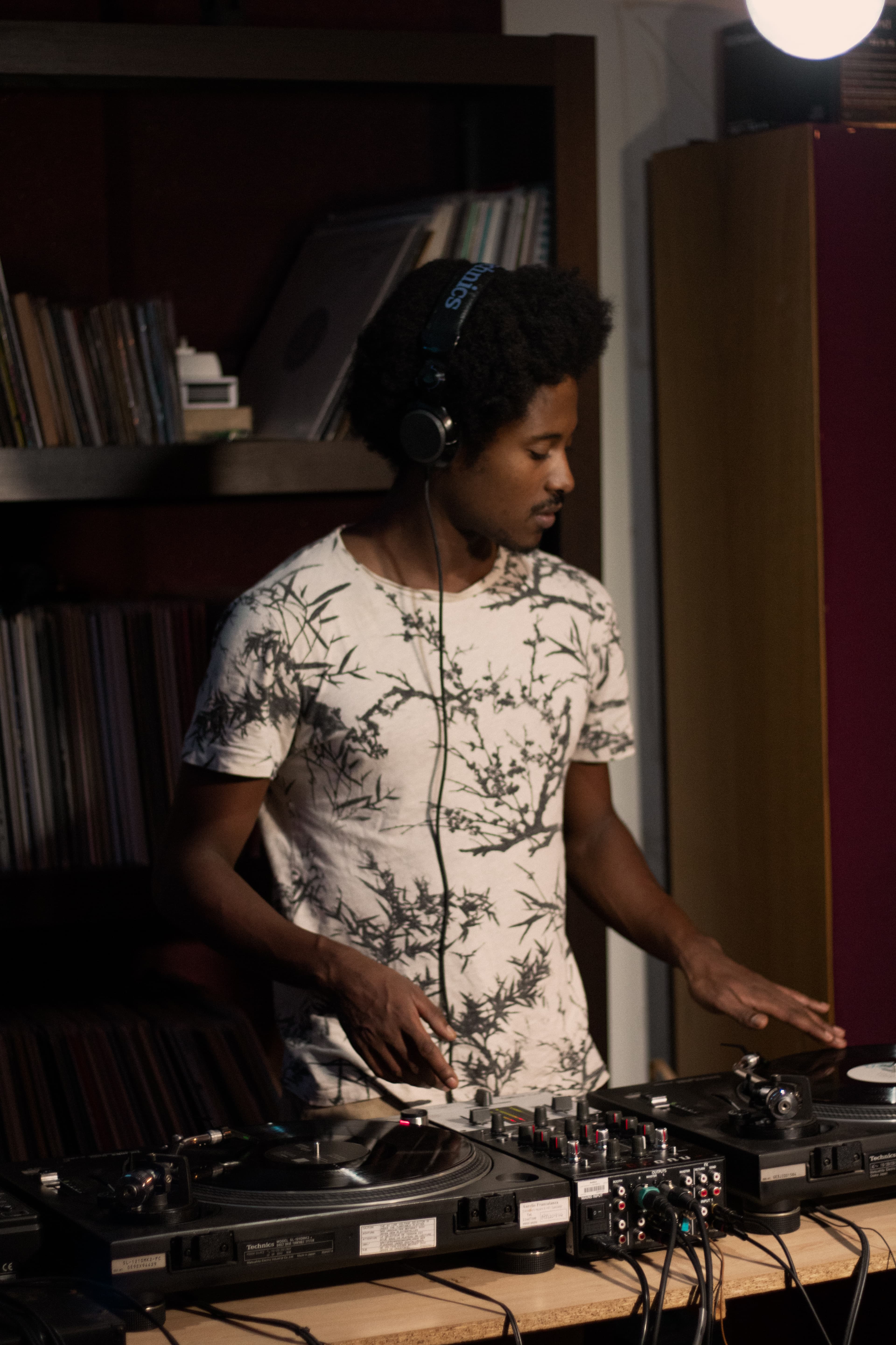 A tutor in headphones mixing on turntables in front of shelves packed with vinyl records during a one-to-one session